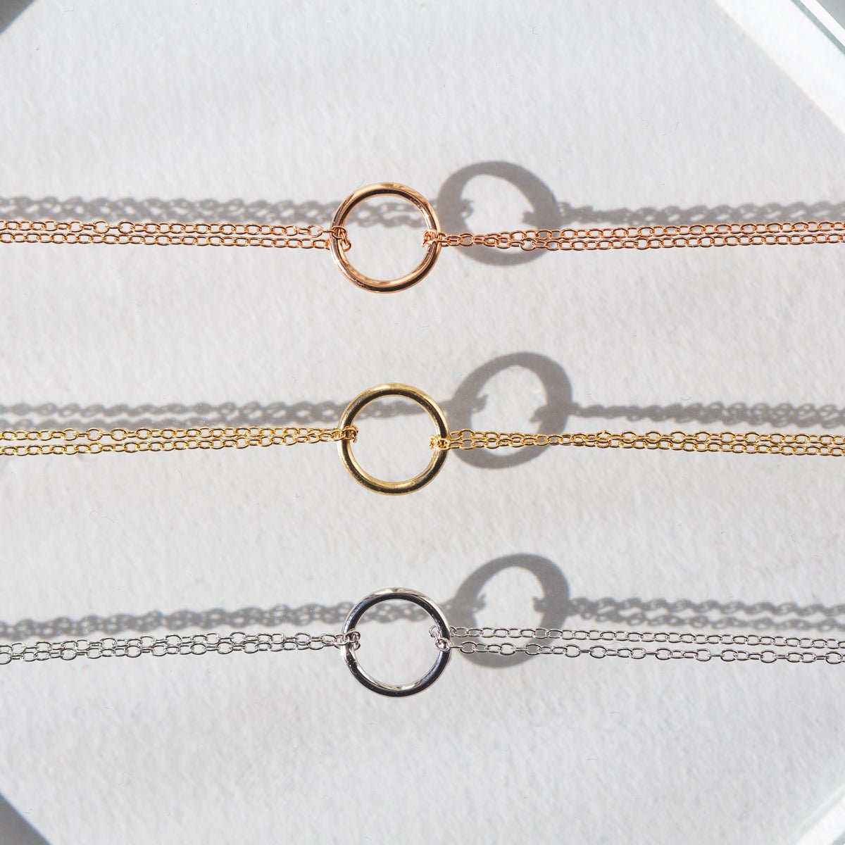 Rose gold, gold, and silver eternity circle chain bracelets lined up on a white background
