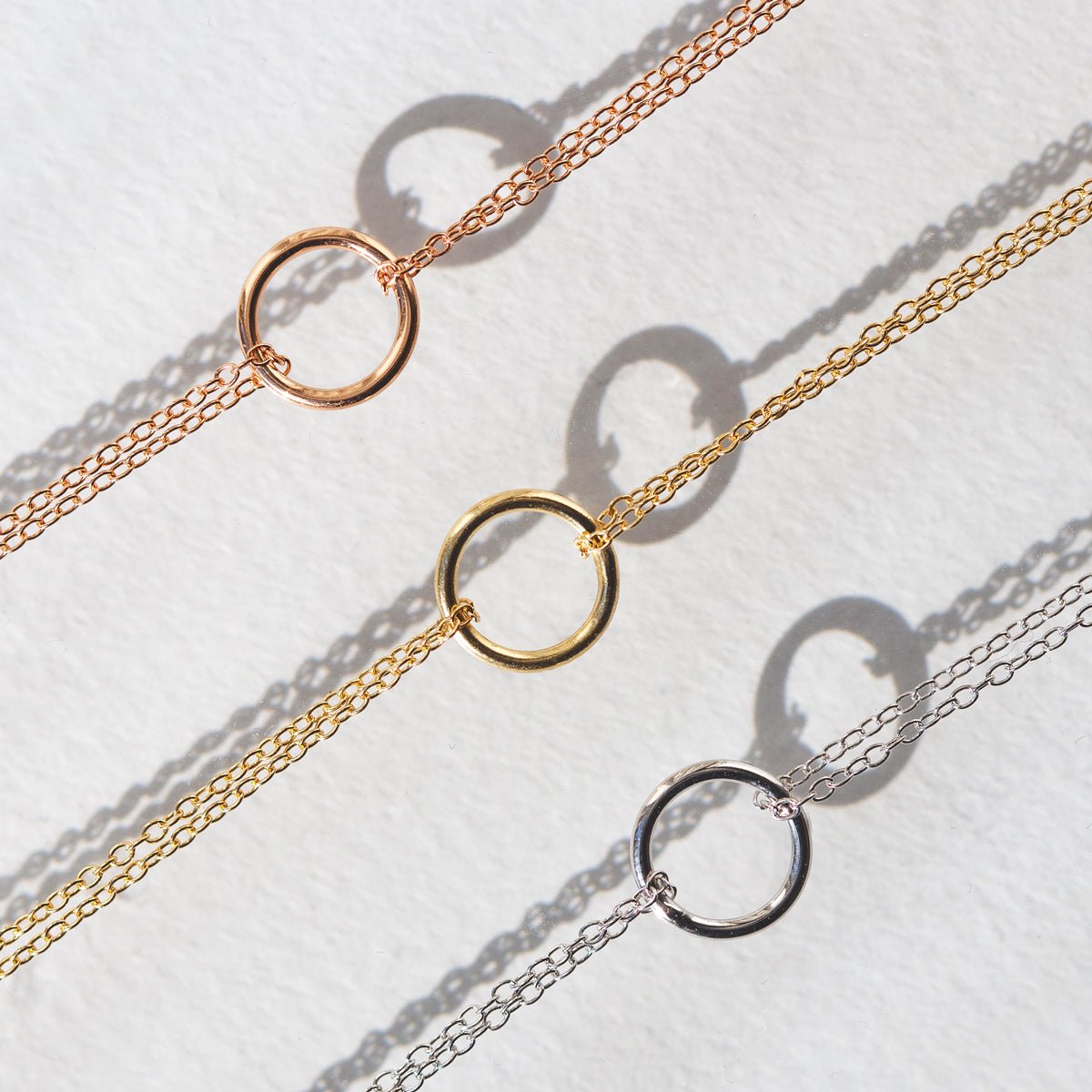 Rose, yellow and silver eternity circle bracelets with open circles, laid on cream paper