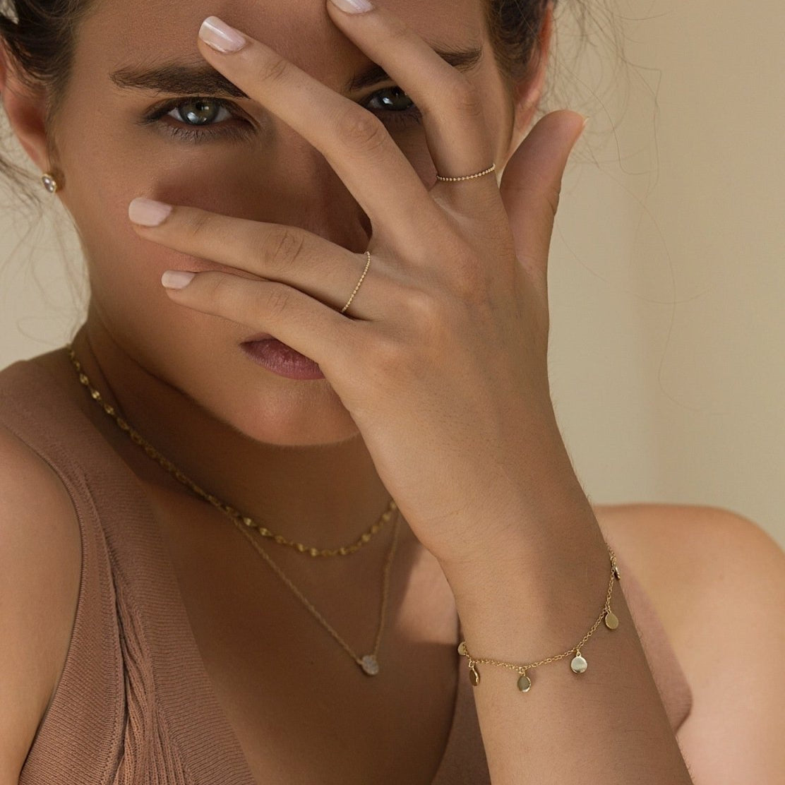 Gold vermeil disc dangle bracelet worn on a model's wrist, shown near the face