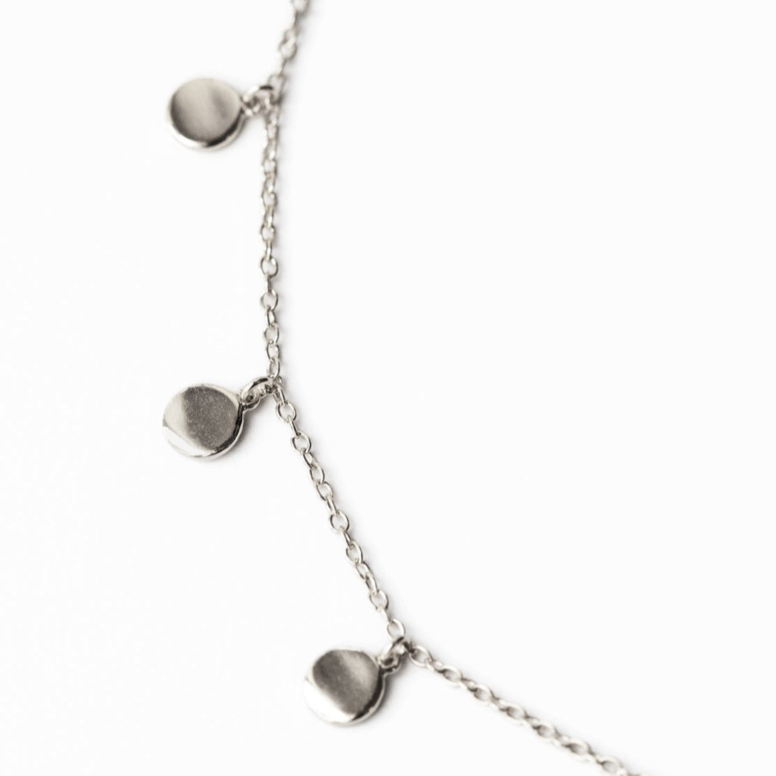 Sterling silver bracelet, close-up detail of round disc charms on a fine chain, on a white background