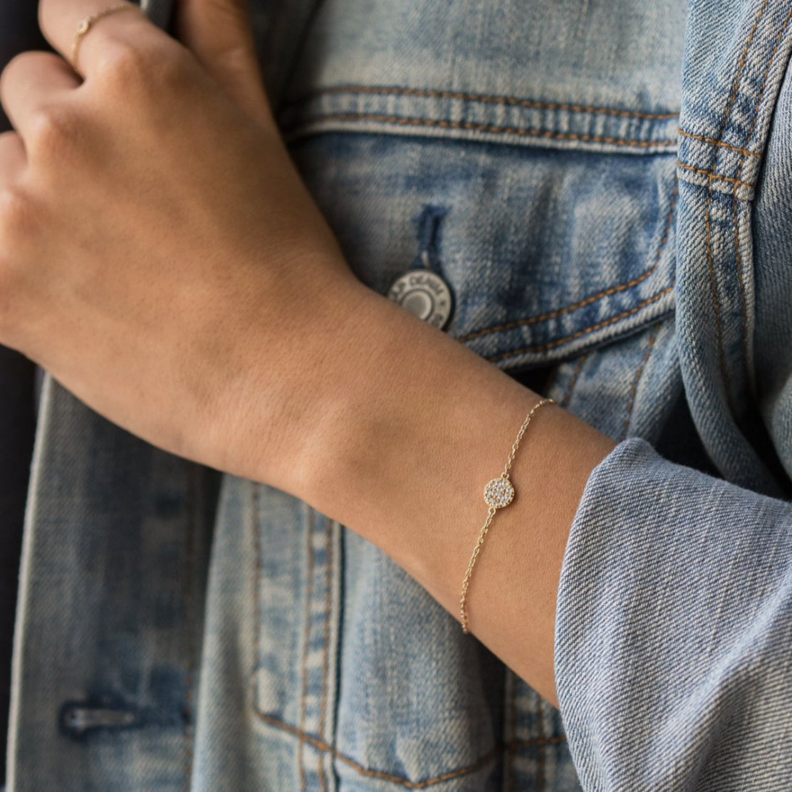 Gold vermeil pavé disc chain bracelet with white zirconia, shown on a model's wrist with denim