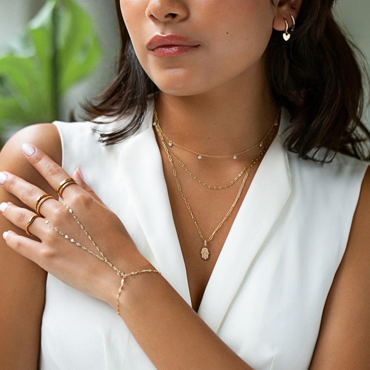 Gold vermeil white zirconia hand chain shown on a model's hand with stacked rings and necklaces