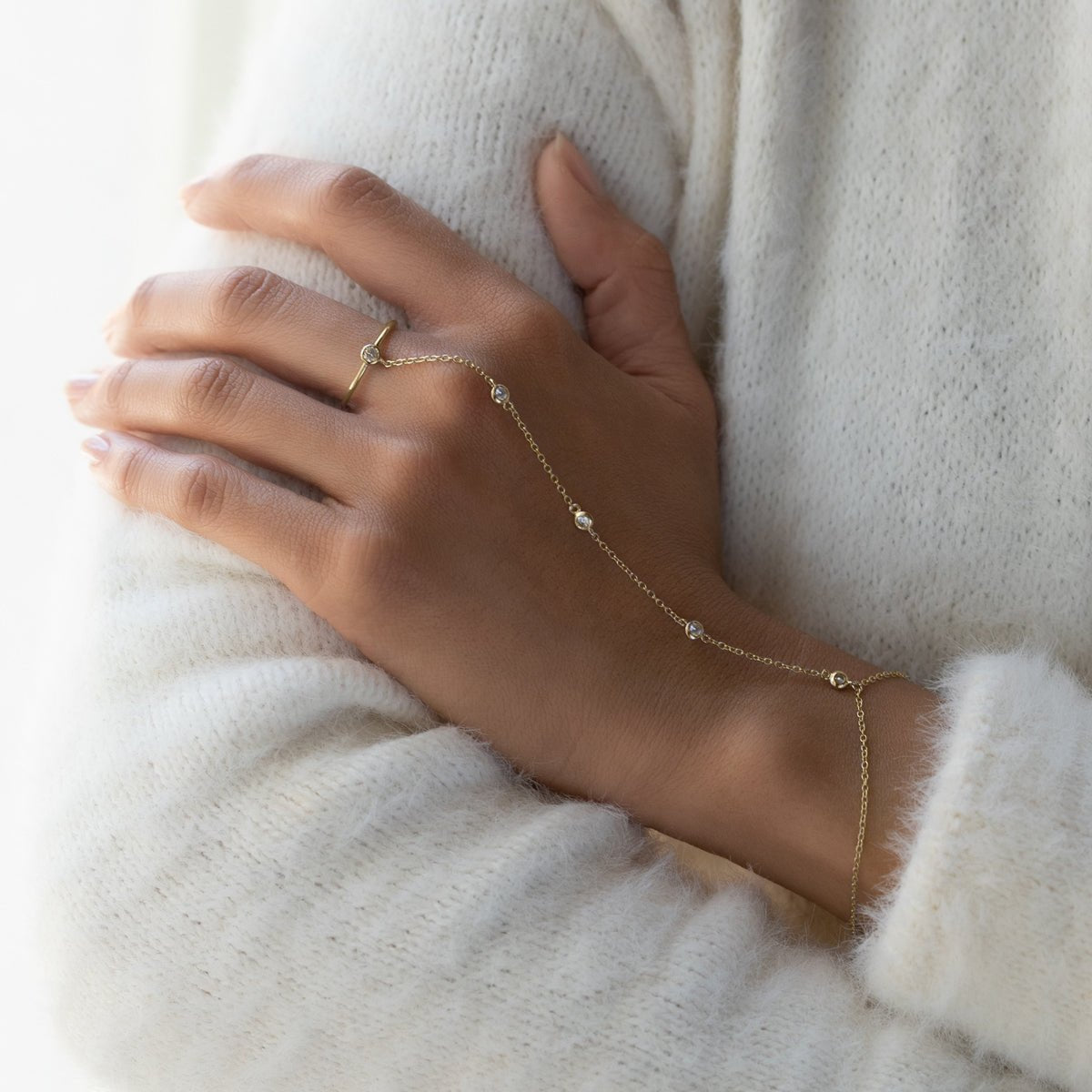 Gold vermeil hand chain with clear stones and a ring, shown on a model's hand