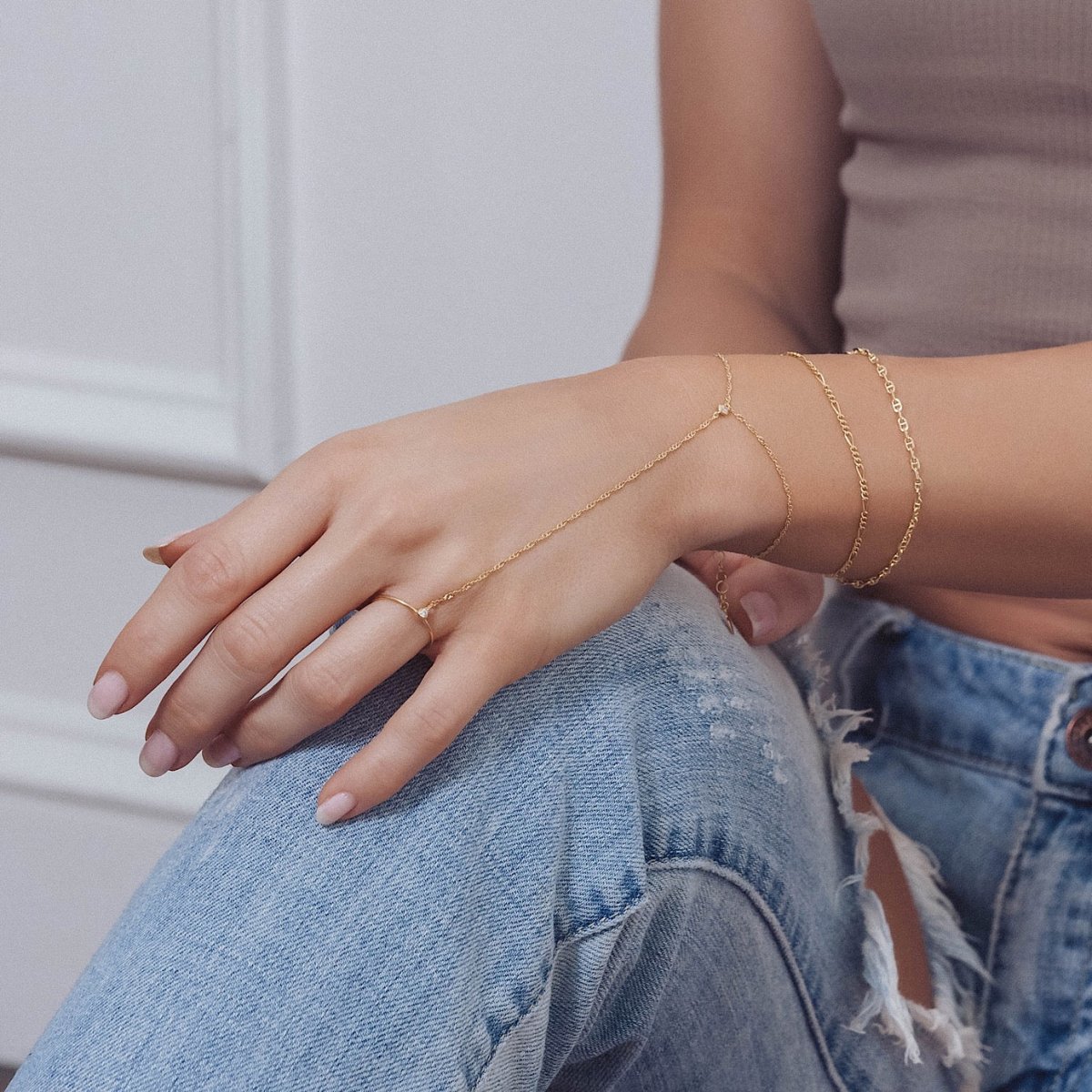 Gold vermeil Figaro chain bracelet layered with delicate chains, shown on a seated model's wrist