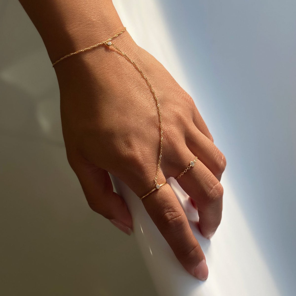 14K gold chain ring with a clear stone, shown on a model's hand with a matching hand chain