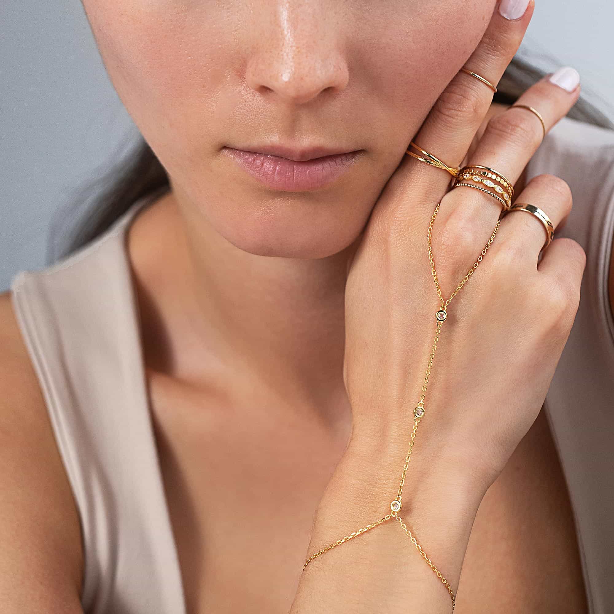 Gold clear-stone hand chain with stacking rings on a model's hand near her face