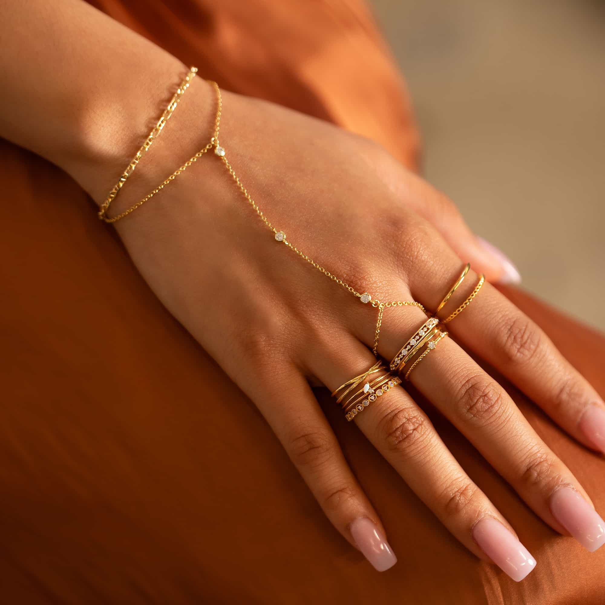 Close-up of woman wearing gold dainty crystal handchain, gold marina chain bracelet, gold rope double band stacking ring, gold tiny opal double band ring, gold duet rope stacking ring, gold tiny opal eternity stacking ring, and gold gemstone eternity stacking ring