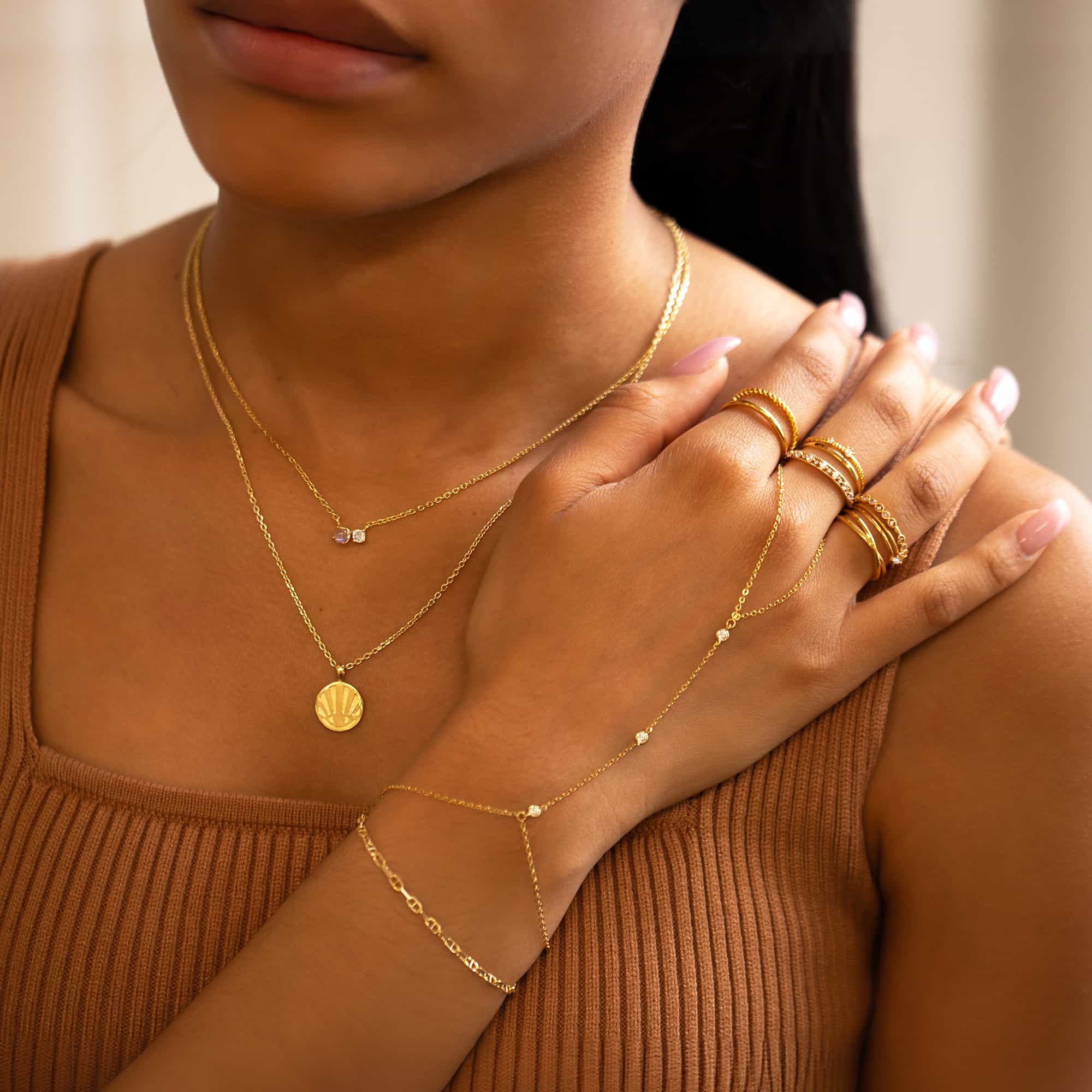 Gold vermeil round sunburst rays pendant necklace layered with chains, shown on a model's neckline