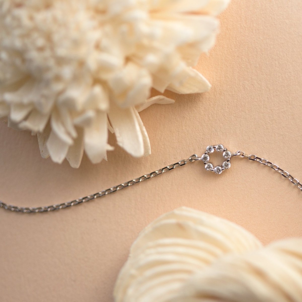 Sterling silver chain bracelet with a zirconia open circle, laid on cream beside a flower