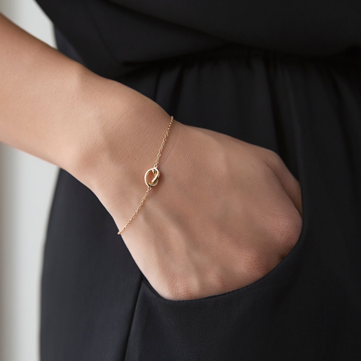 Gold vermeil love knot bracelet shown on a model's wrist against a black dress