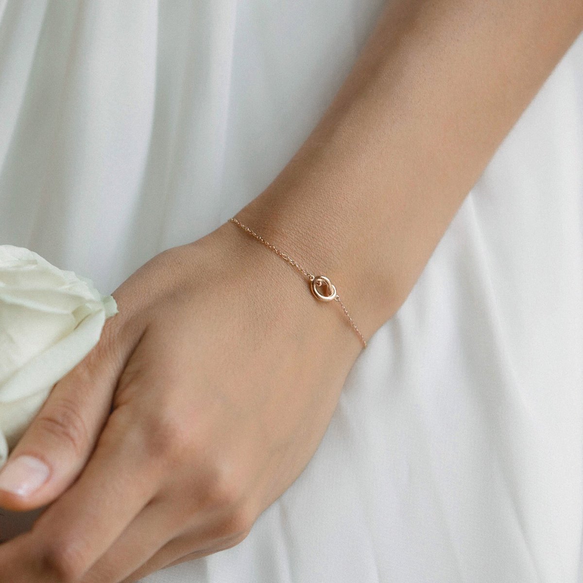 Rose gold vermeil love knot bracelet shown on a model's wrist against white fabric