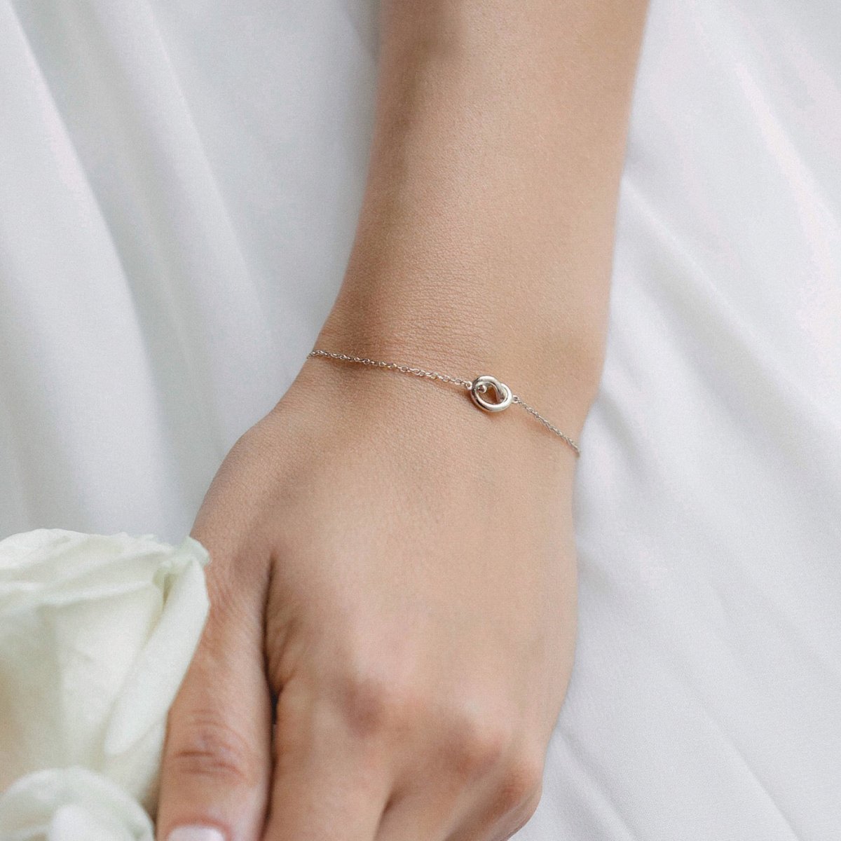 Sterling silver love knot bracelet shown on a model's wrist against white fabric