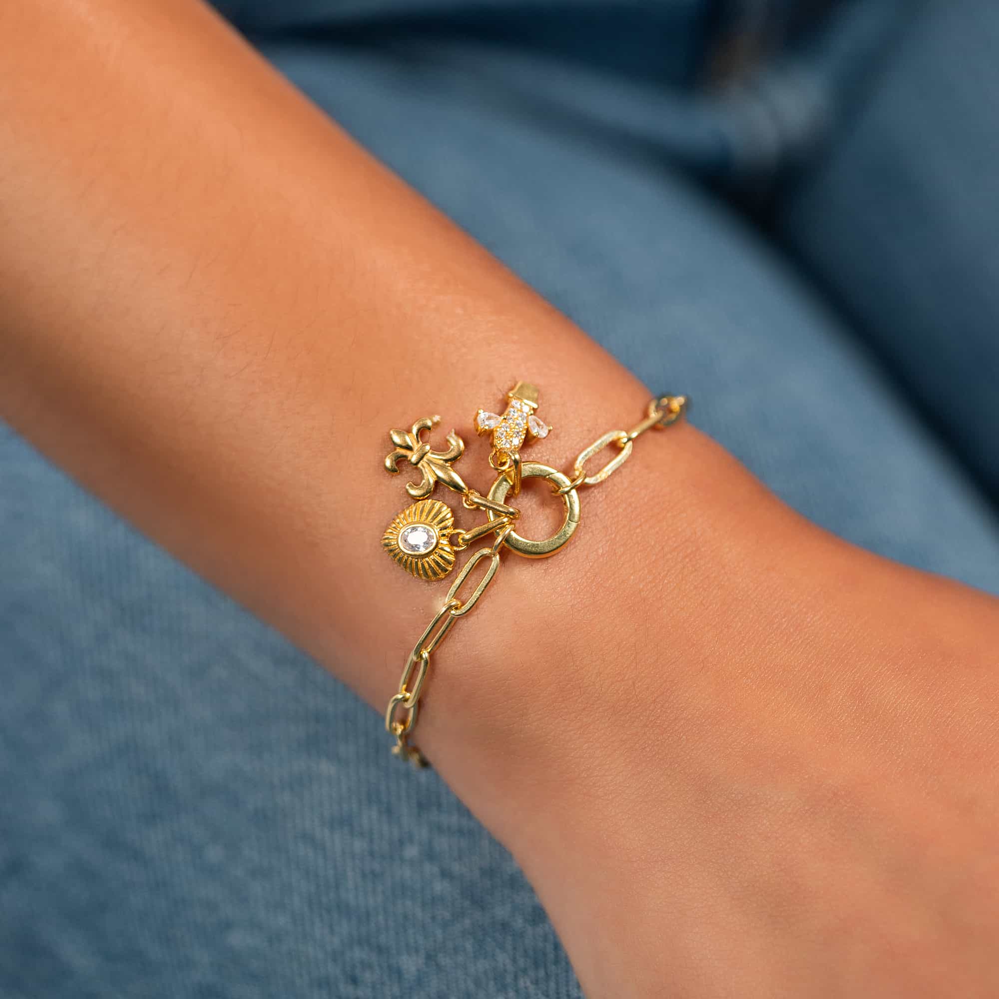 Gold charm bracelet with clustered charms and a clear stone heart, on a model's wrist