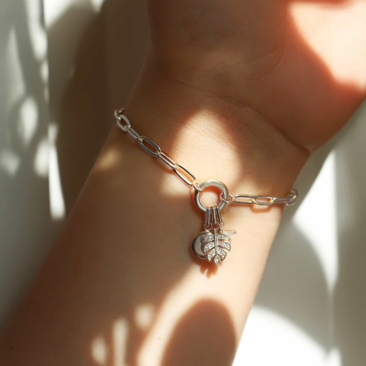 Sterling silver monstera leaf charm on a paperclip chain bracelet, shown on a model's wrist