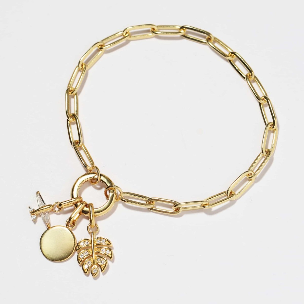 Gold vermeil paperclip chain charm bracelet with a clasp ring, pave leaf and disc charms, on a white background