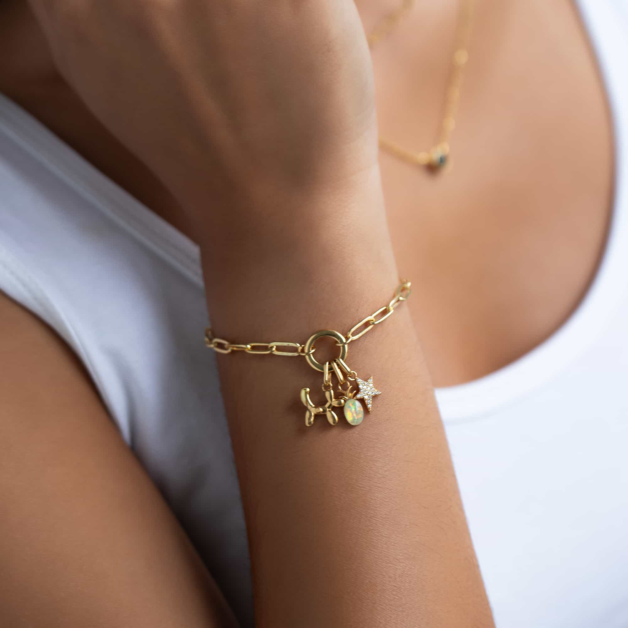 Gold paperclip chain bracelet with a balloon dog, opal and pave star charm cluster, on a model's wrist