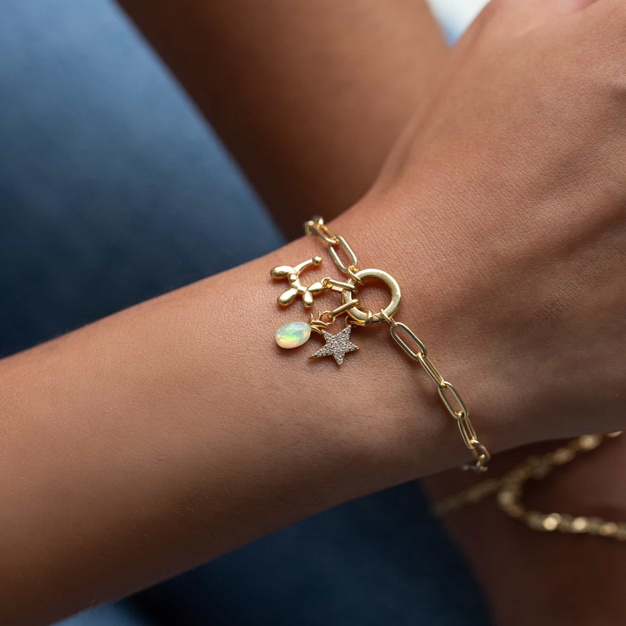 Gold paperclip chain bracelet with a balloon dog, opal, star and other charms, on a model's wrist