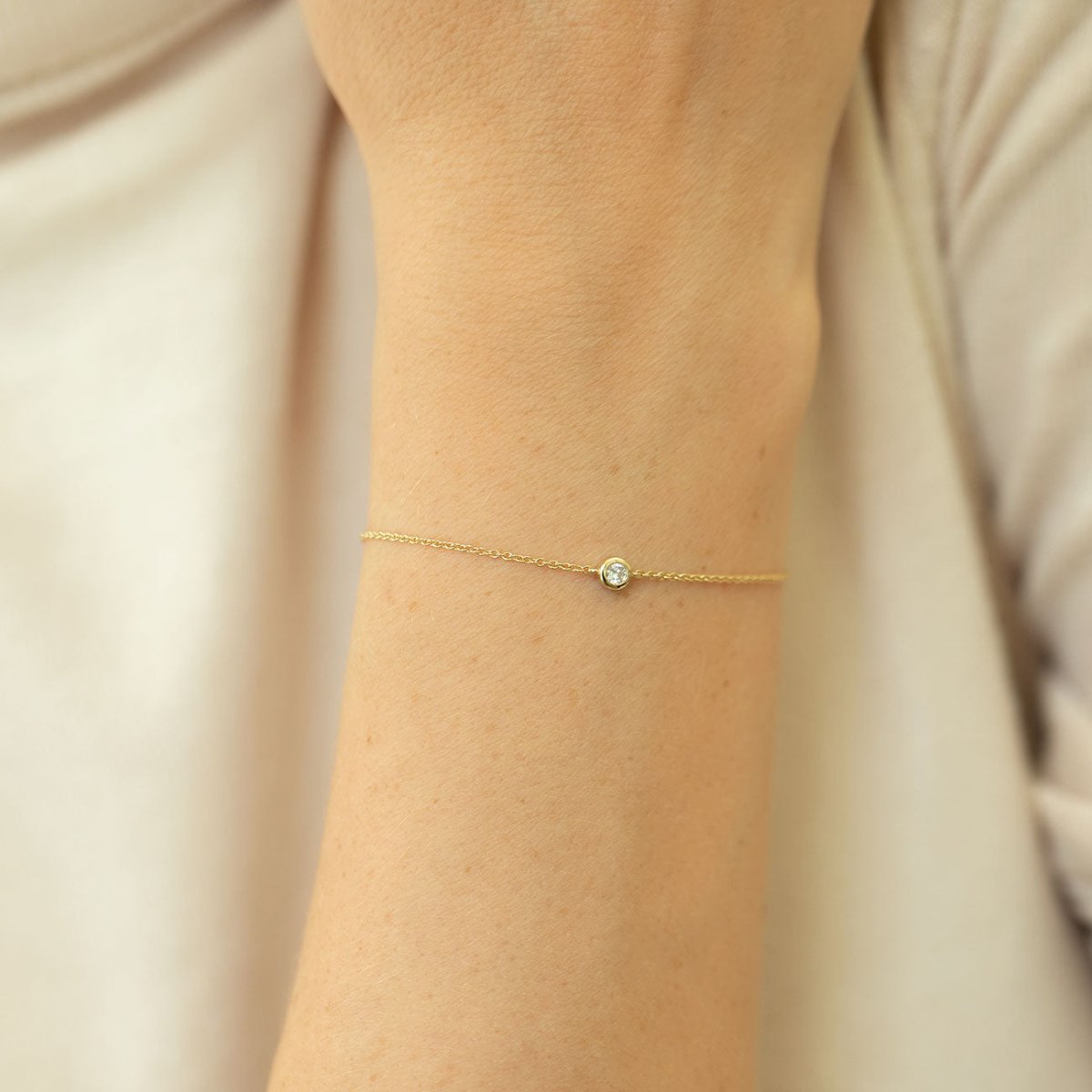 14K gold bezel diamond chain bracelet shown on a model's wrist over cream fabric