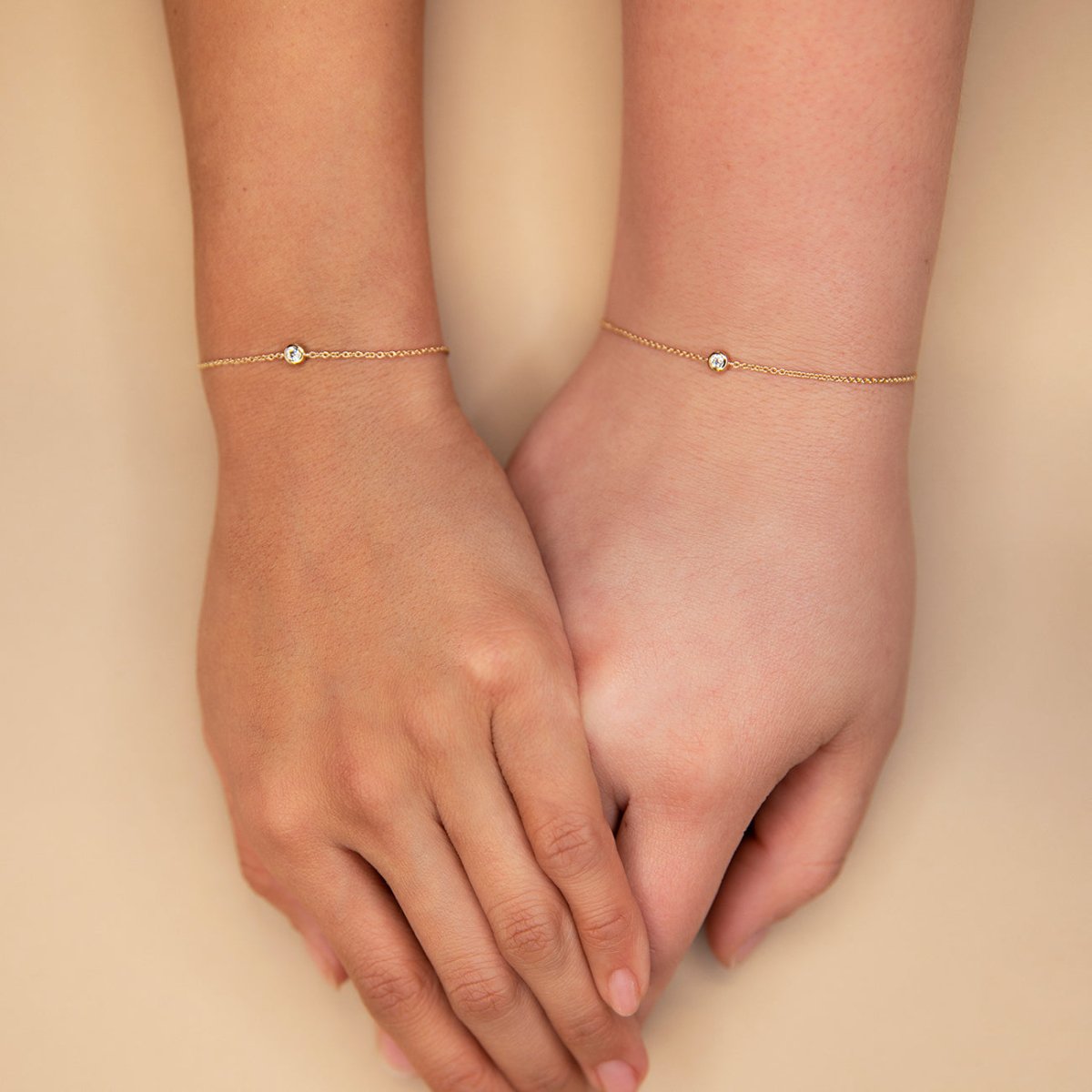 14K gold bezel diamond chain bracelets shown on two model wrists on a cream background