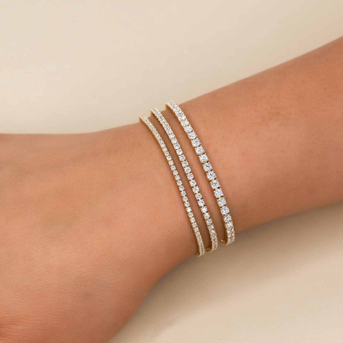14K gold diamond tennis bracelets stacked on a model's wrist, on a cream background