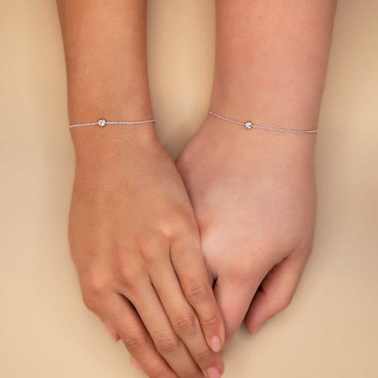 14K white gold bezel diamond chain bracelets shown on two model wrists on a cream background