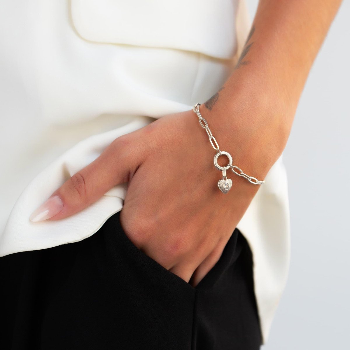 Sterling silver heart charm with a clear stone on a ring-clasp paperclip bracelet, on a model's wrist