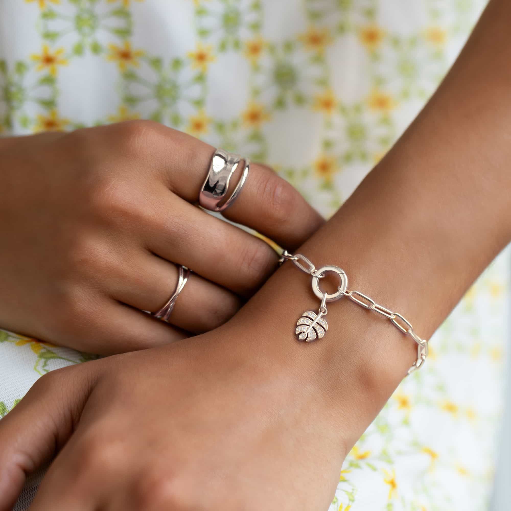 Silver wrap ring and a paperclip-chain bracelet with a pavé leaf charm, shown on a model's hands