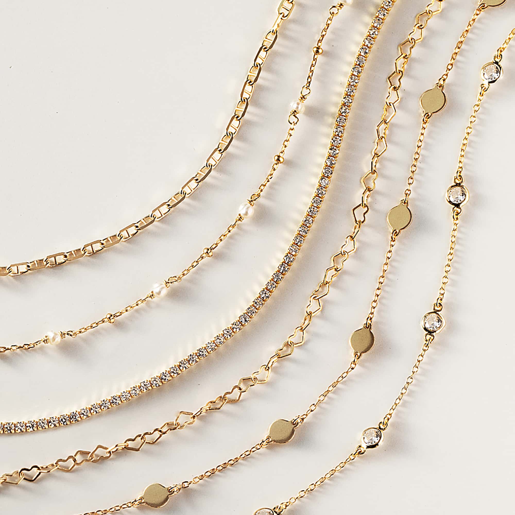 Assorted gold chain bracelets, including paperclip and clear-stone styles, on a cream background