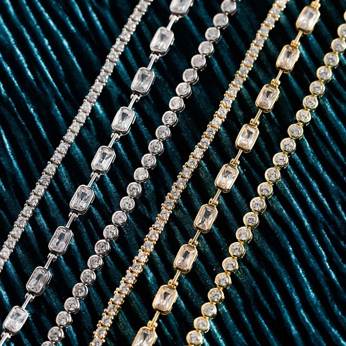 Close-up of gold and silver crystal tennis bracelets with white zirconia, laid on dark green velvet