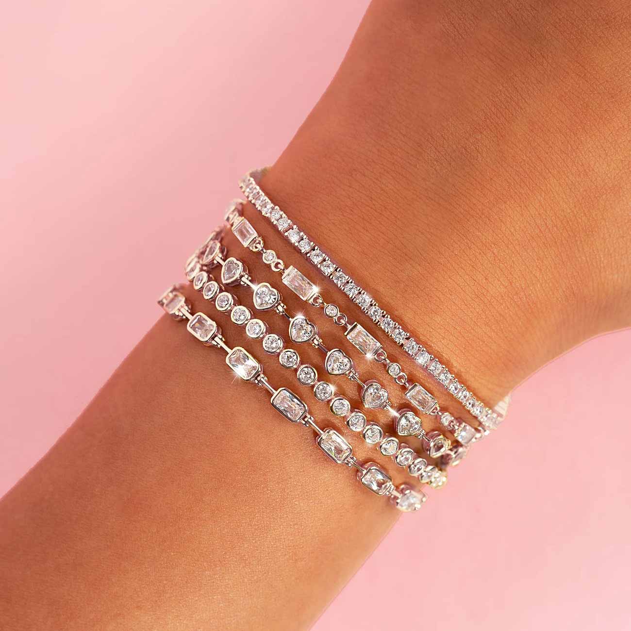 Silver tennis bracelets with mixed-cut clear stones, stacked on a model's wrist on pink