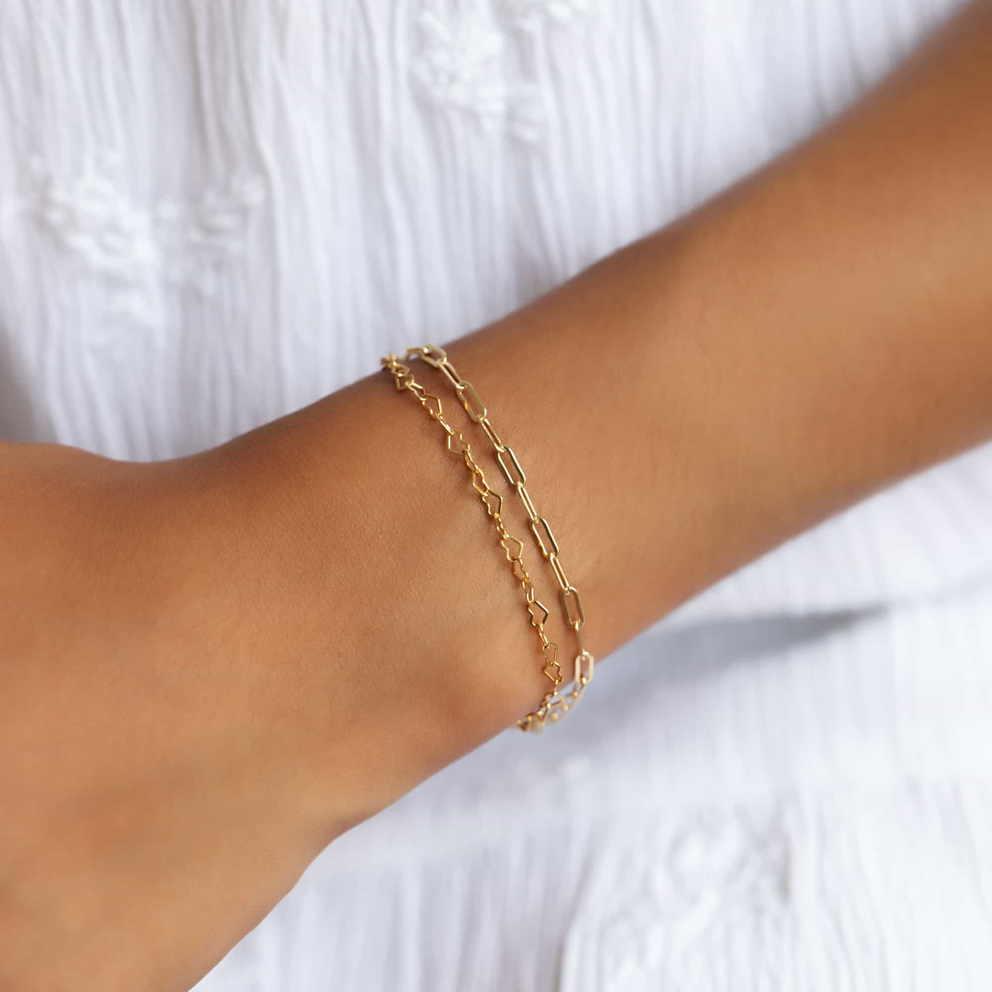 Two layered gold chain bracelets in different link styles on a model's wrist