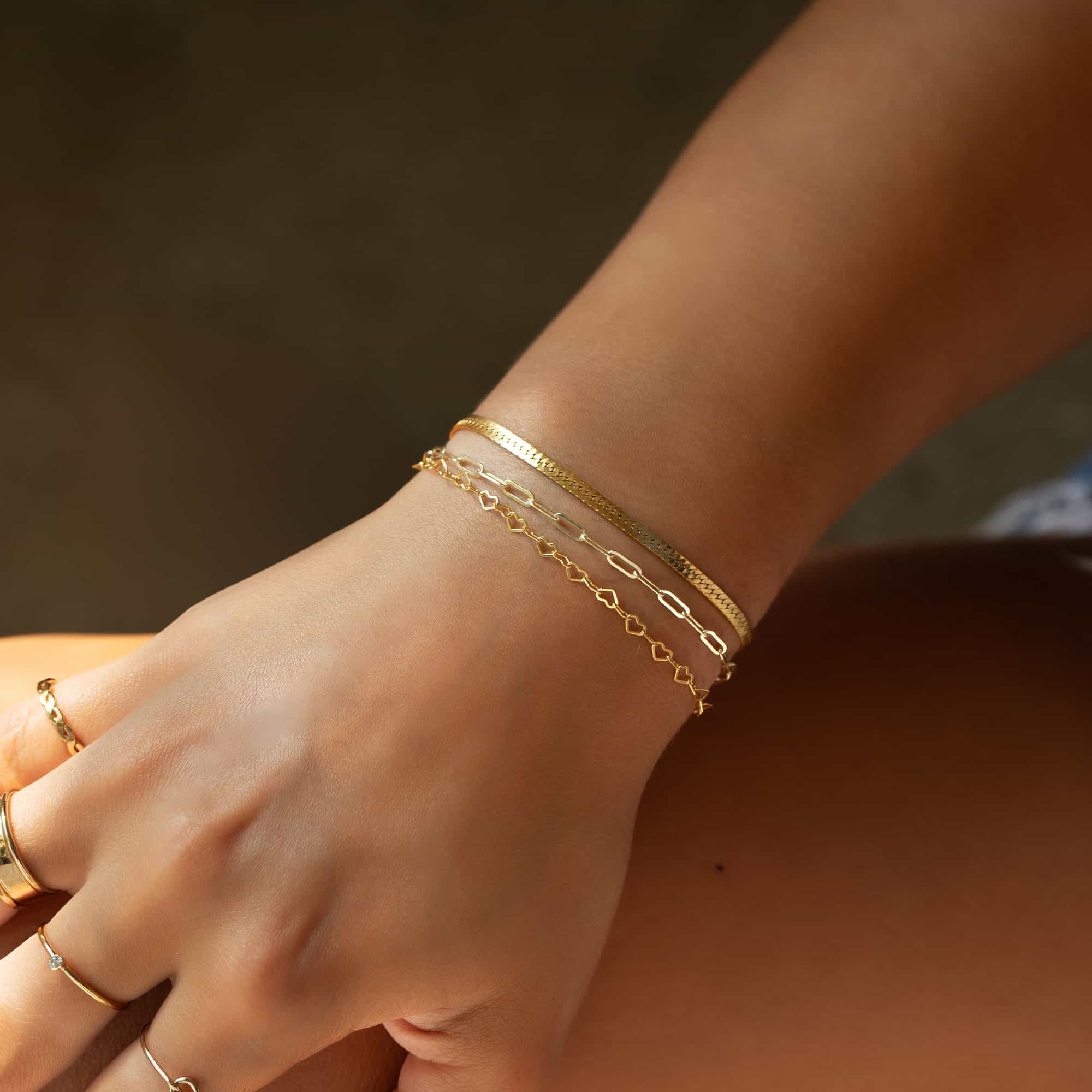 Gold-filled heart-link chain bracelet layered with a paperclip chain, shown on a model's wrist