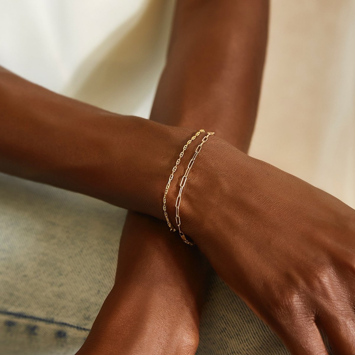14K gold thin paperclip chain bracelet layered on a model's wrist, close on the arm