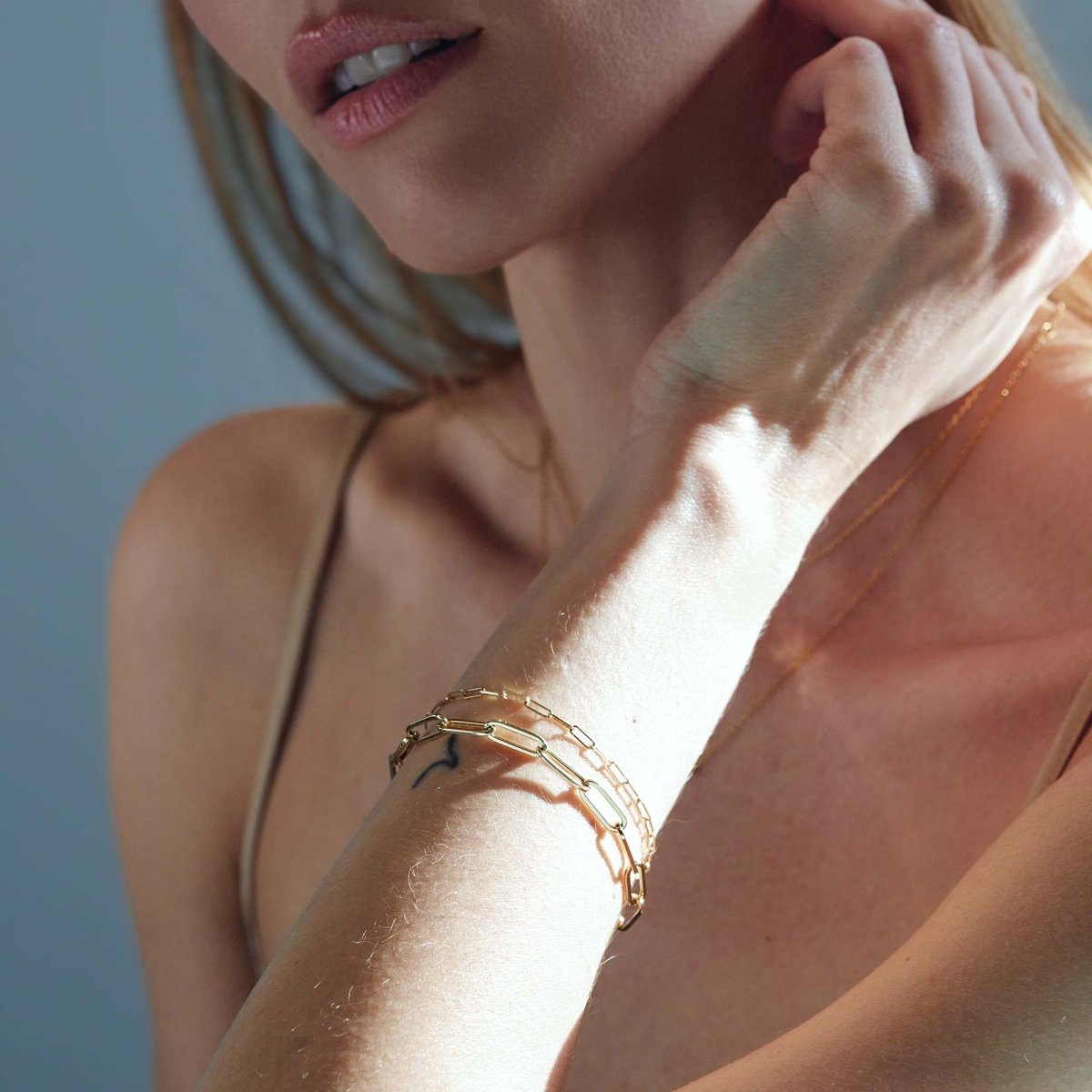 14K gold paperclip chain bracelets layered on a model's wrist held near her neckline