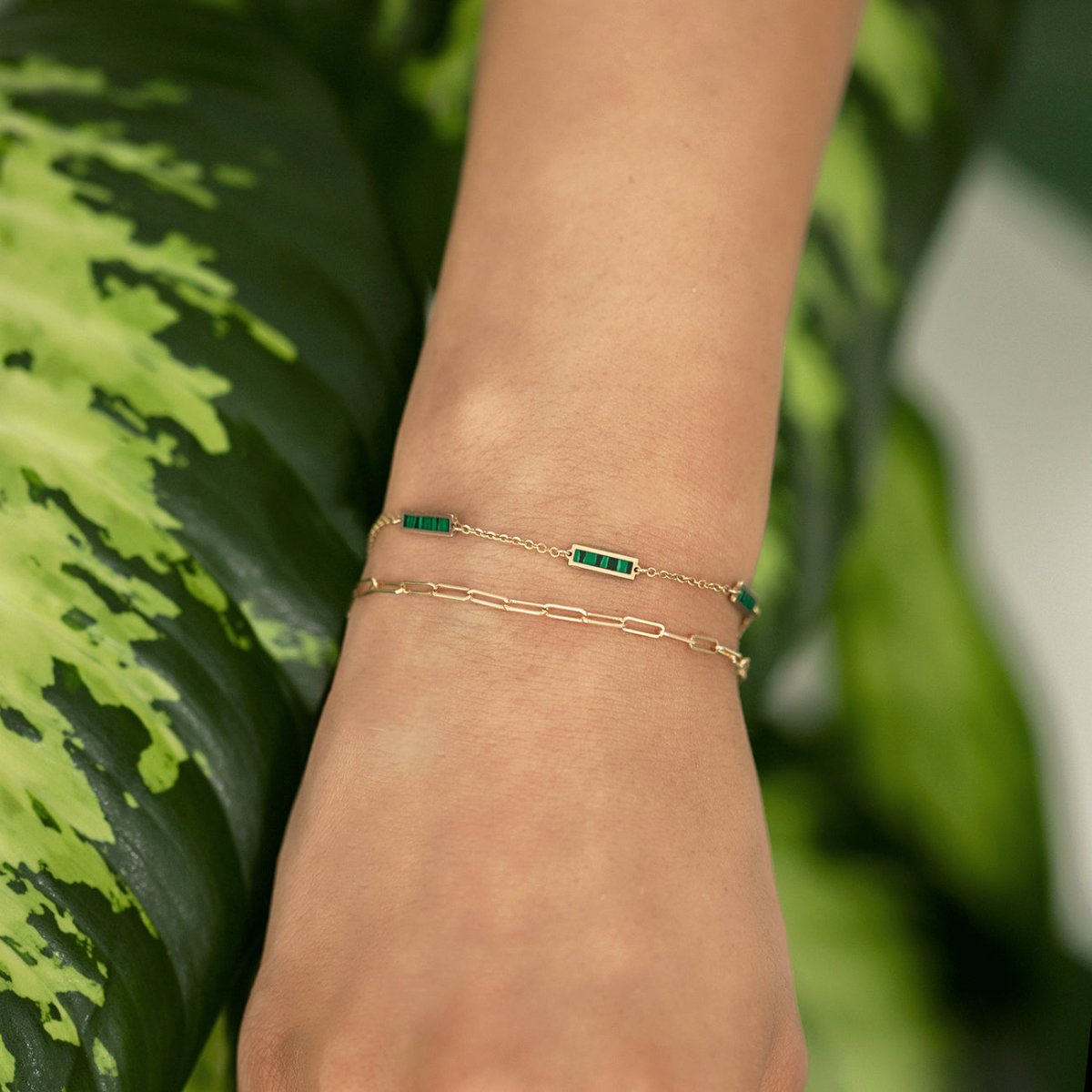 14K gold malachite bar bracelet shown close on a model's wrist against green leaves