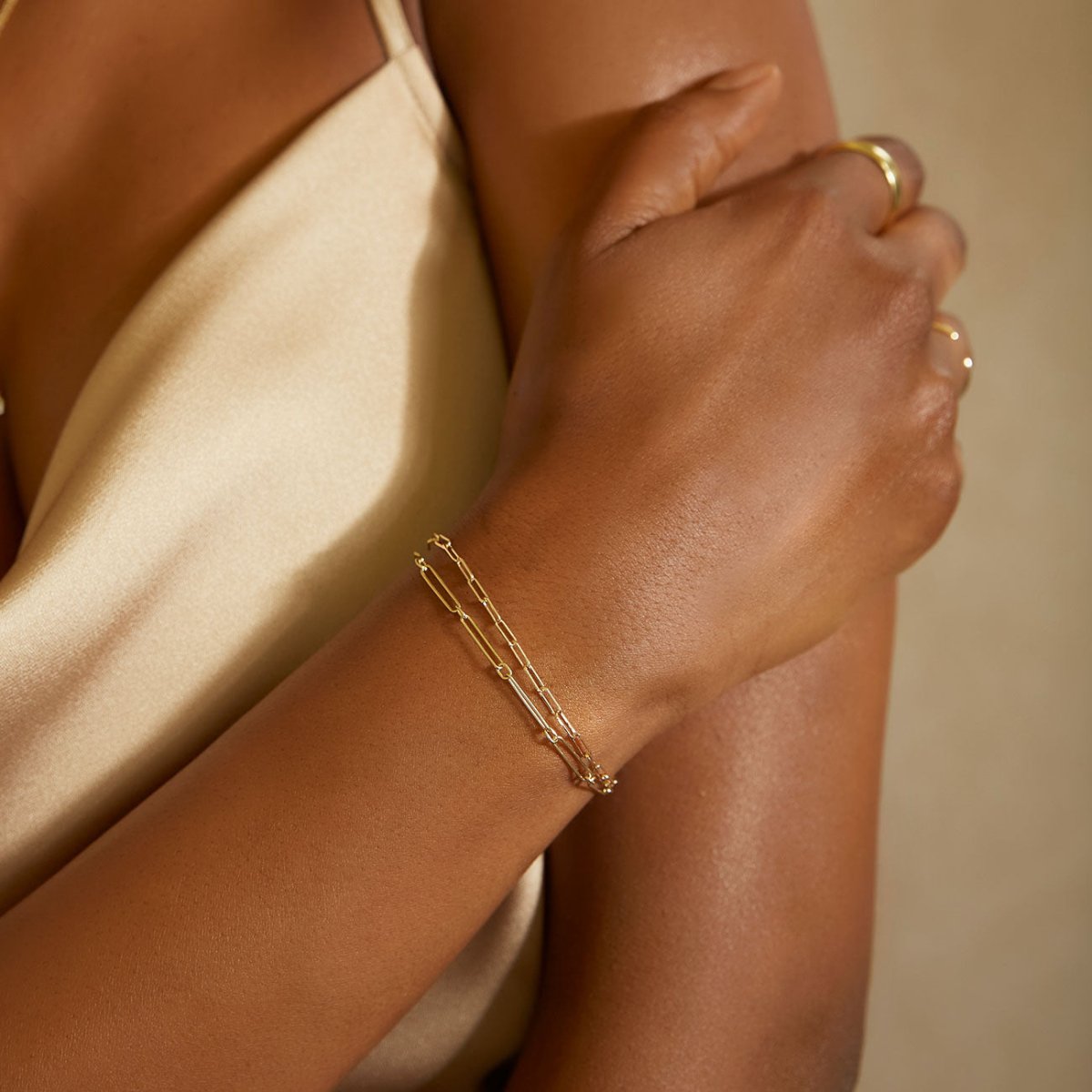 14K gold paperclip chain bracelet on a model's wrist against a cream slip dress