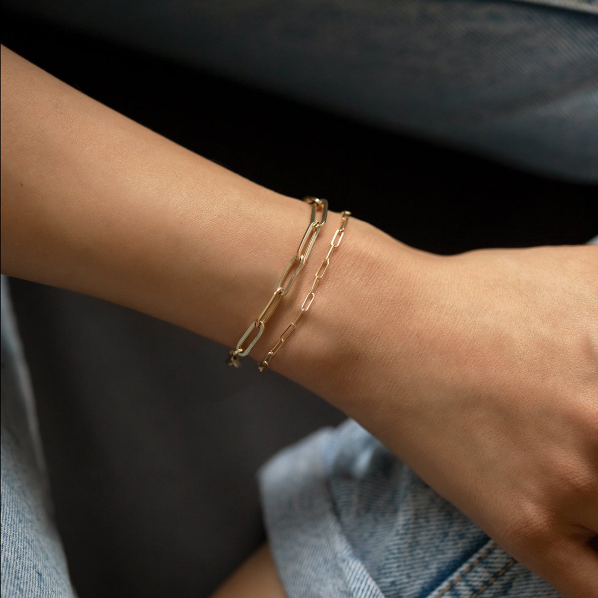 14K gold paperclip chain bracelets shown doubled on a model's wrist against denim