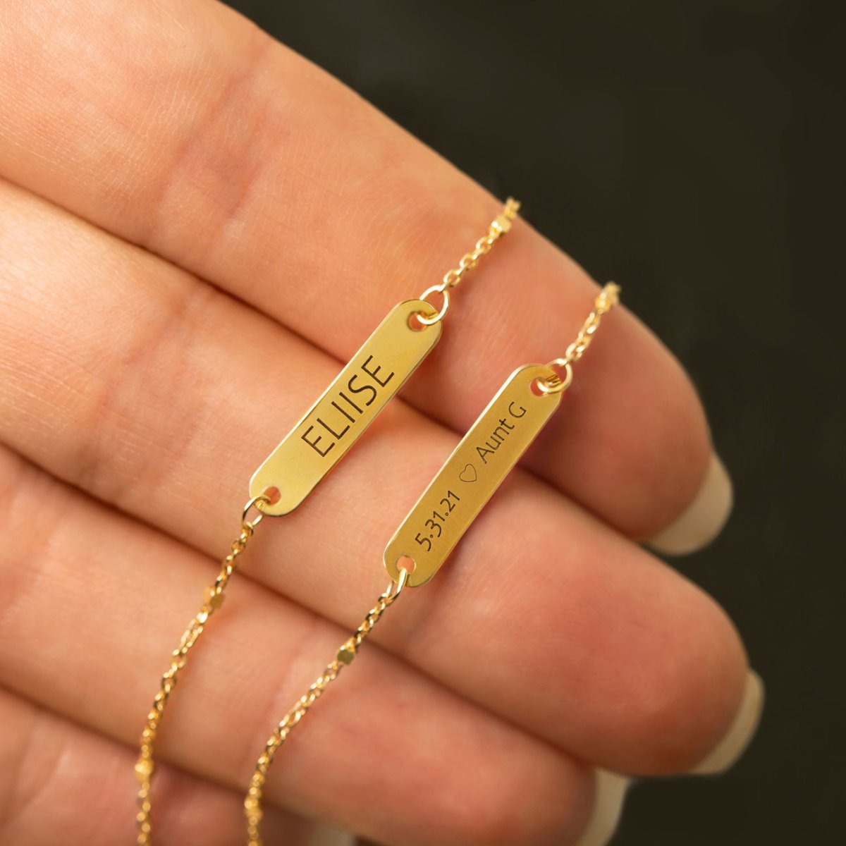 14K gold ID bracelet engraved with a name and date, close-up held in the hand