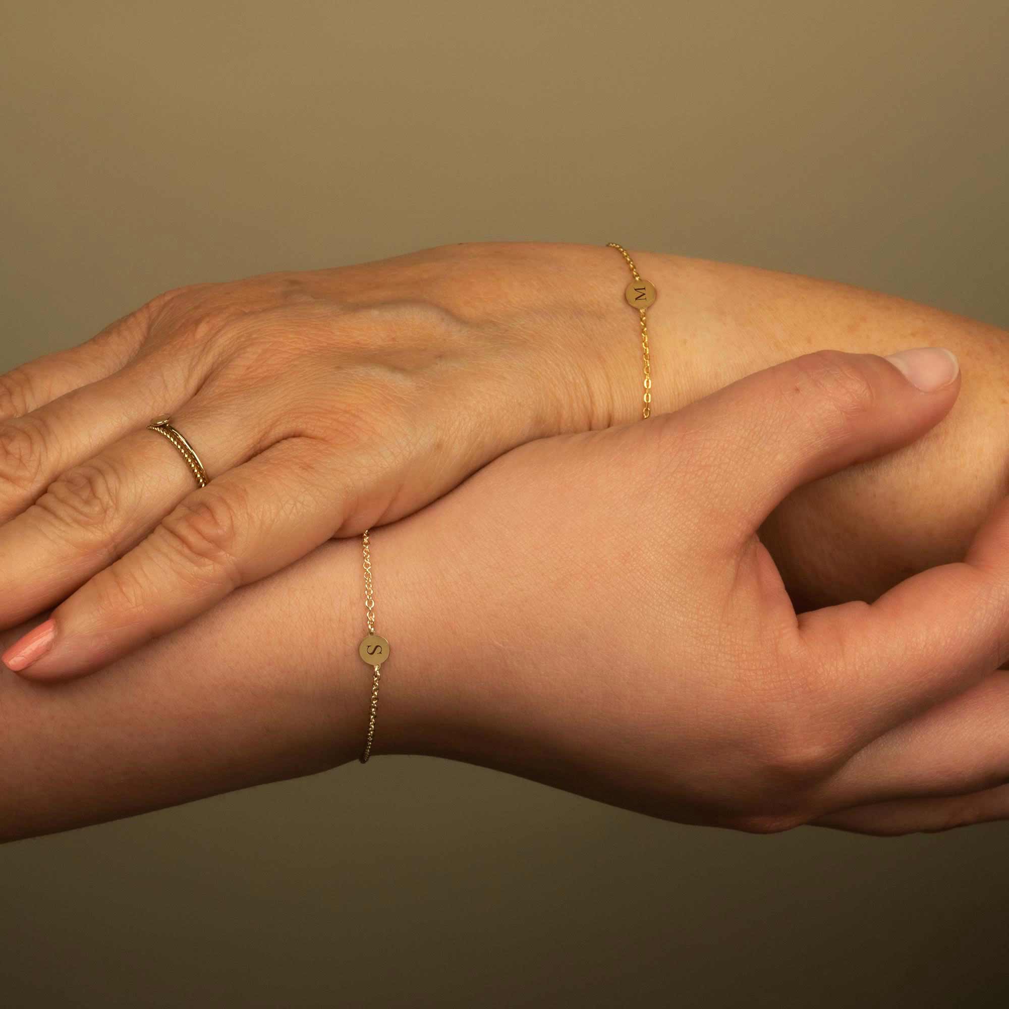 Gold vermeil initial disc bracelets engraved with a letter, shown on two wrists