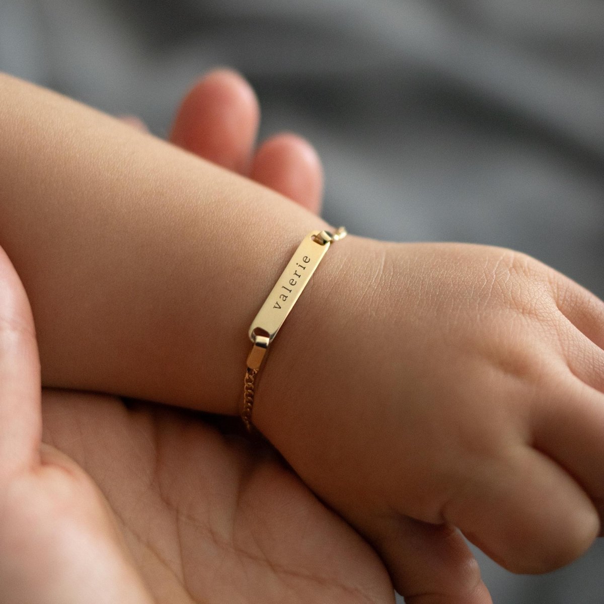 14K gold ID bracelet engraved with a name, shown on a child's wrist held in an adult hand