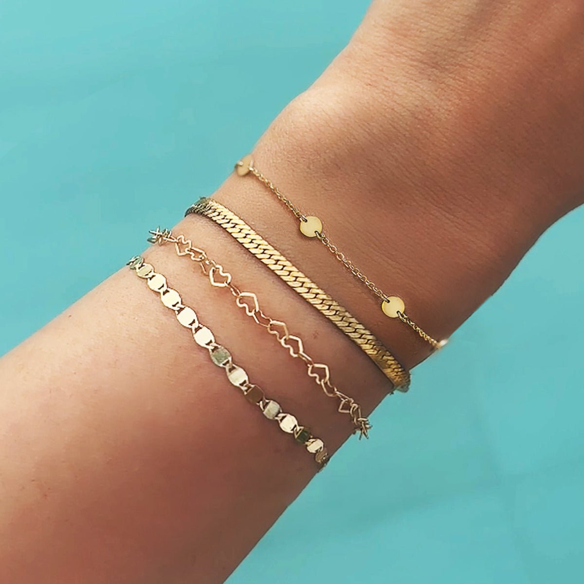 14K gold mirror chain bracelet stacked on a model's wrist against a blue background