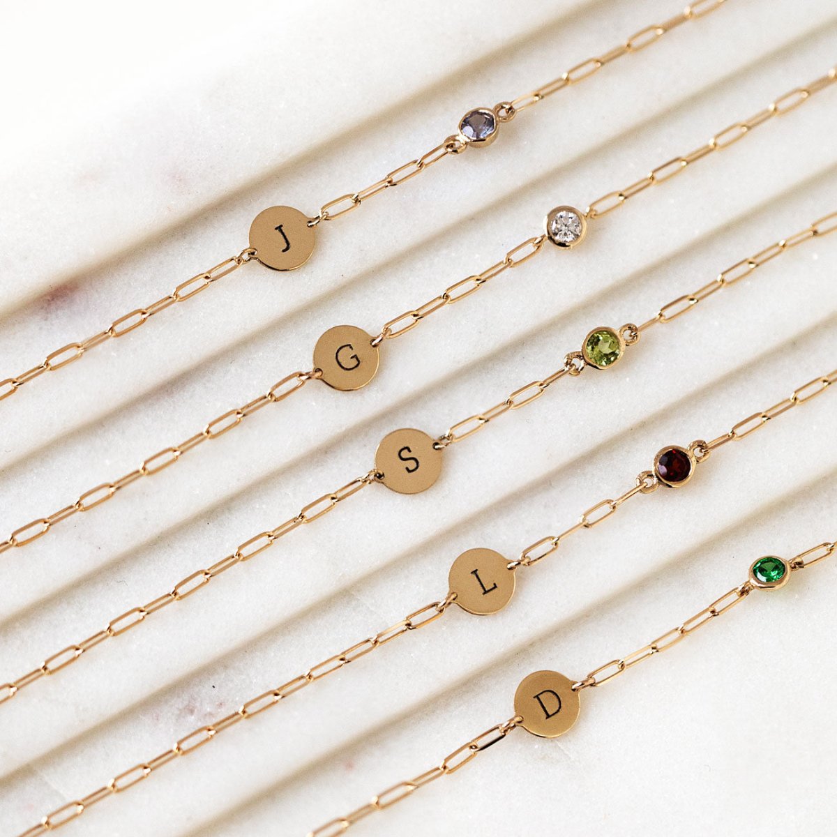 14K gold initial disc bracelets with moissanite and colored stones, stacked on a model's wrist