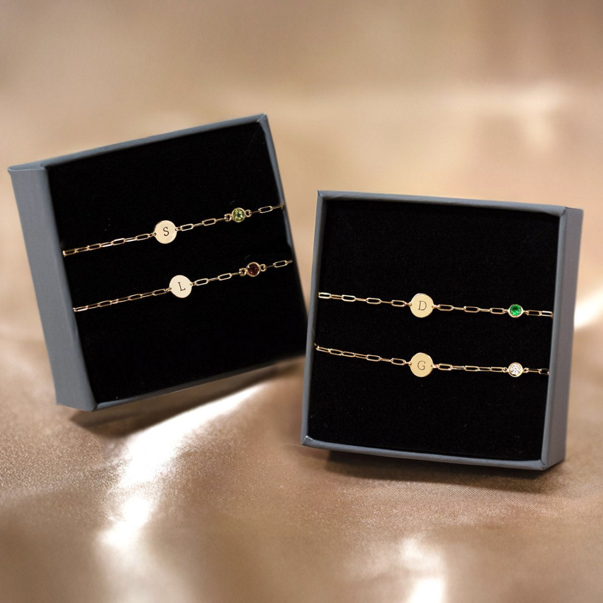 14K gold initial disc bracelets with moissanite and colored stones, laid on white marble