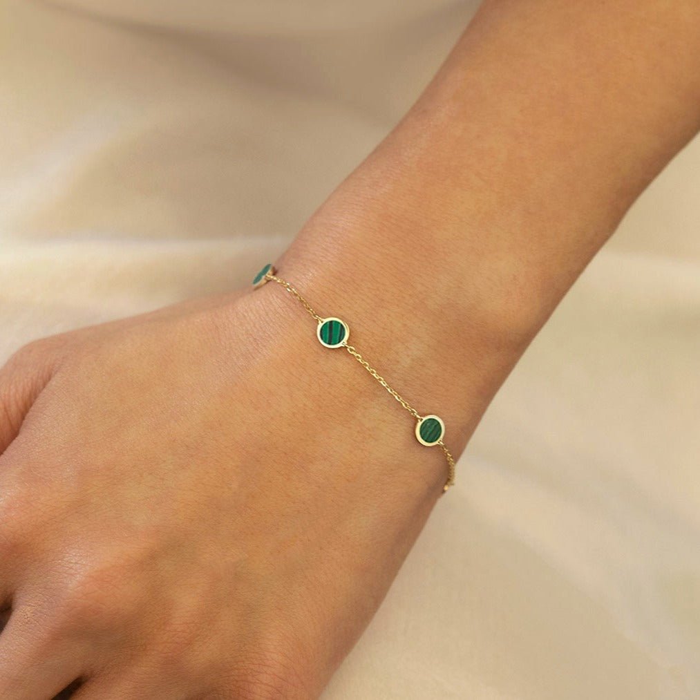 14K gold station bracelet with green malachite discs, close-up on a model's wrist over cream fabric