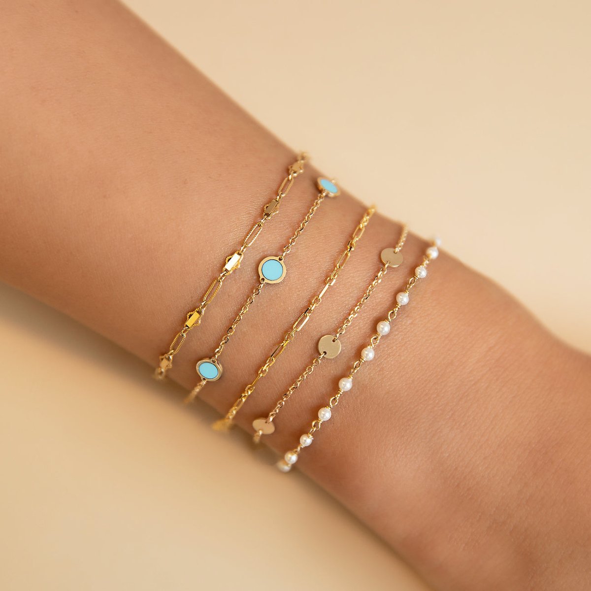 14K gold station bracelets with round turquoise discs, layered and shown on a model's wrist