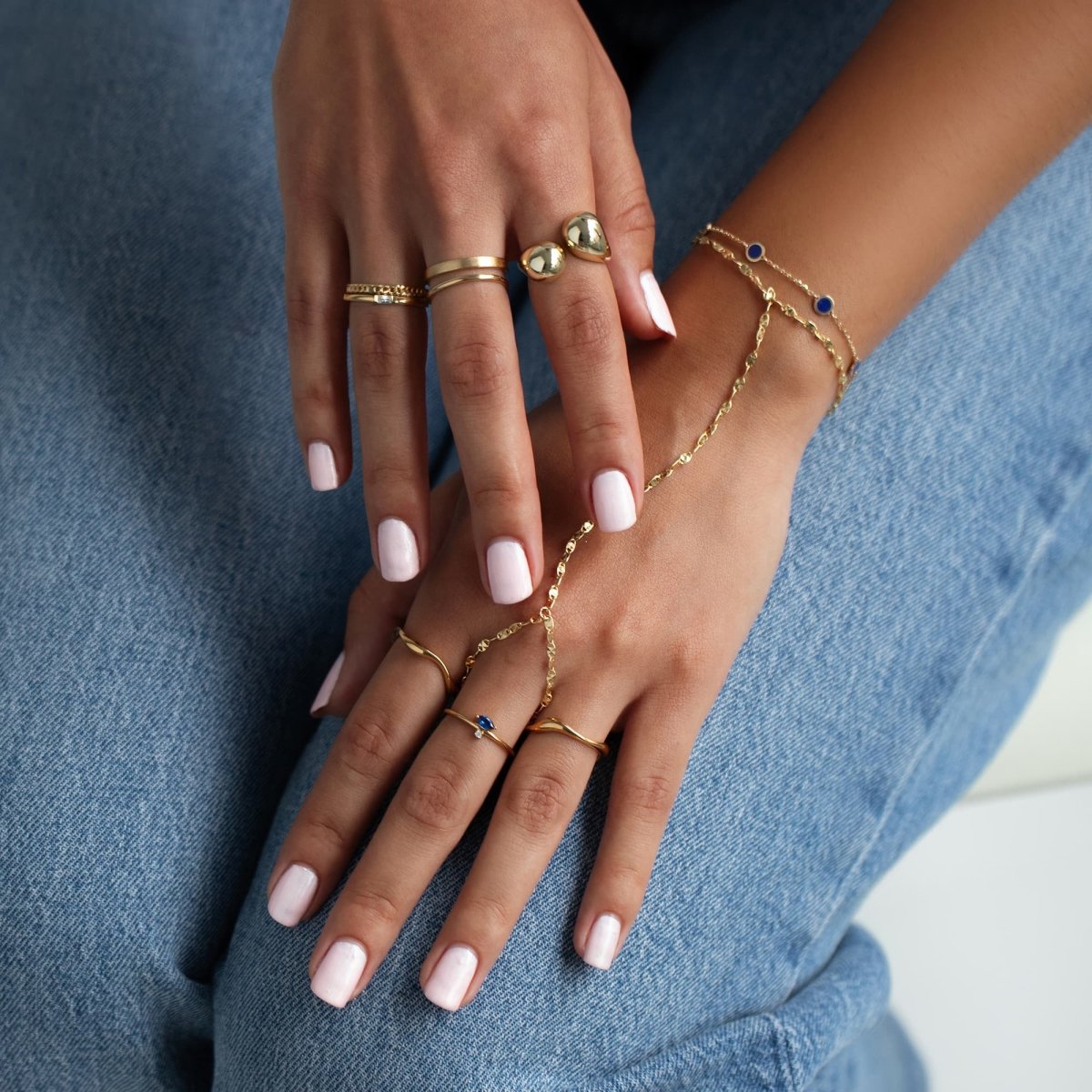 14K gold station bracelet with blue lapis lazuli discs, worn stacked with rings on a model's hand
