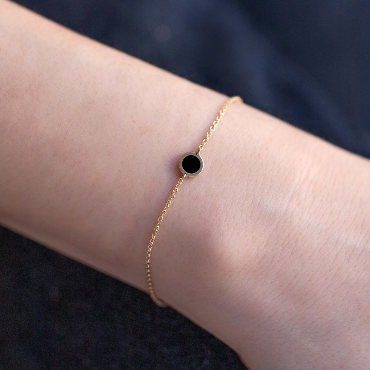14K gold chain bracelet with a small round black onyx stone, close-up on a model's wrist