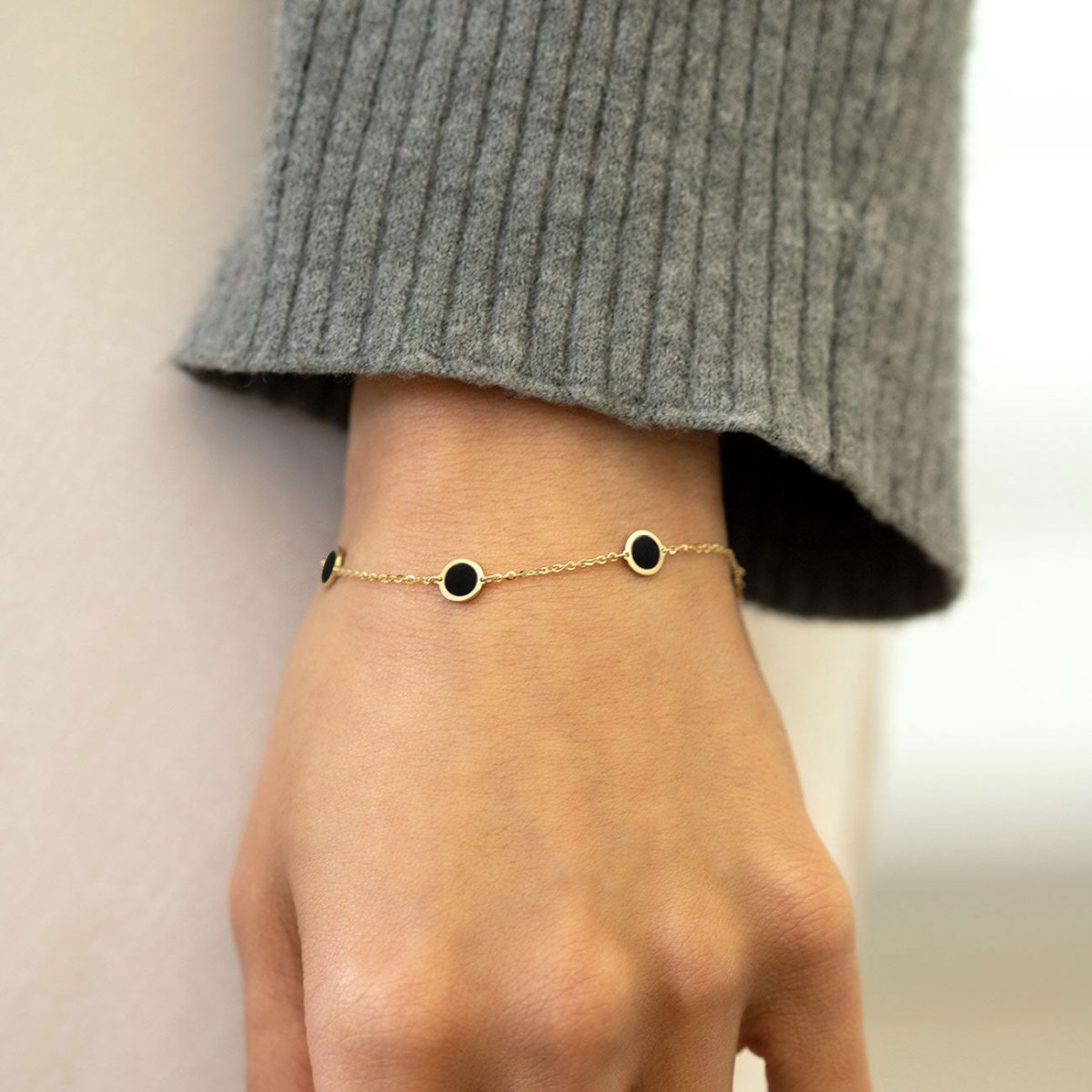 14K gold onyx disc station bracelet shown on a model's wrist below a grey sweater cuff