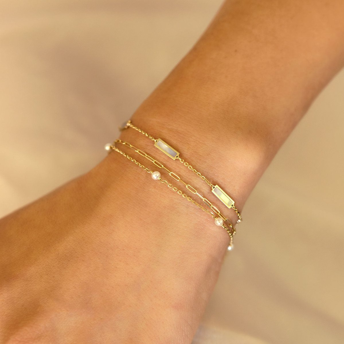 14K gold mother of pearl bar bracelet layered with pearl and paperclip chains on a model's wrist