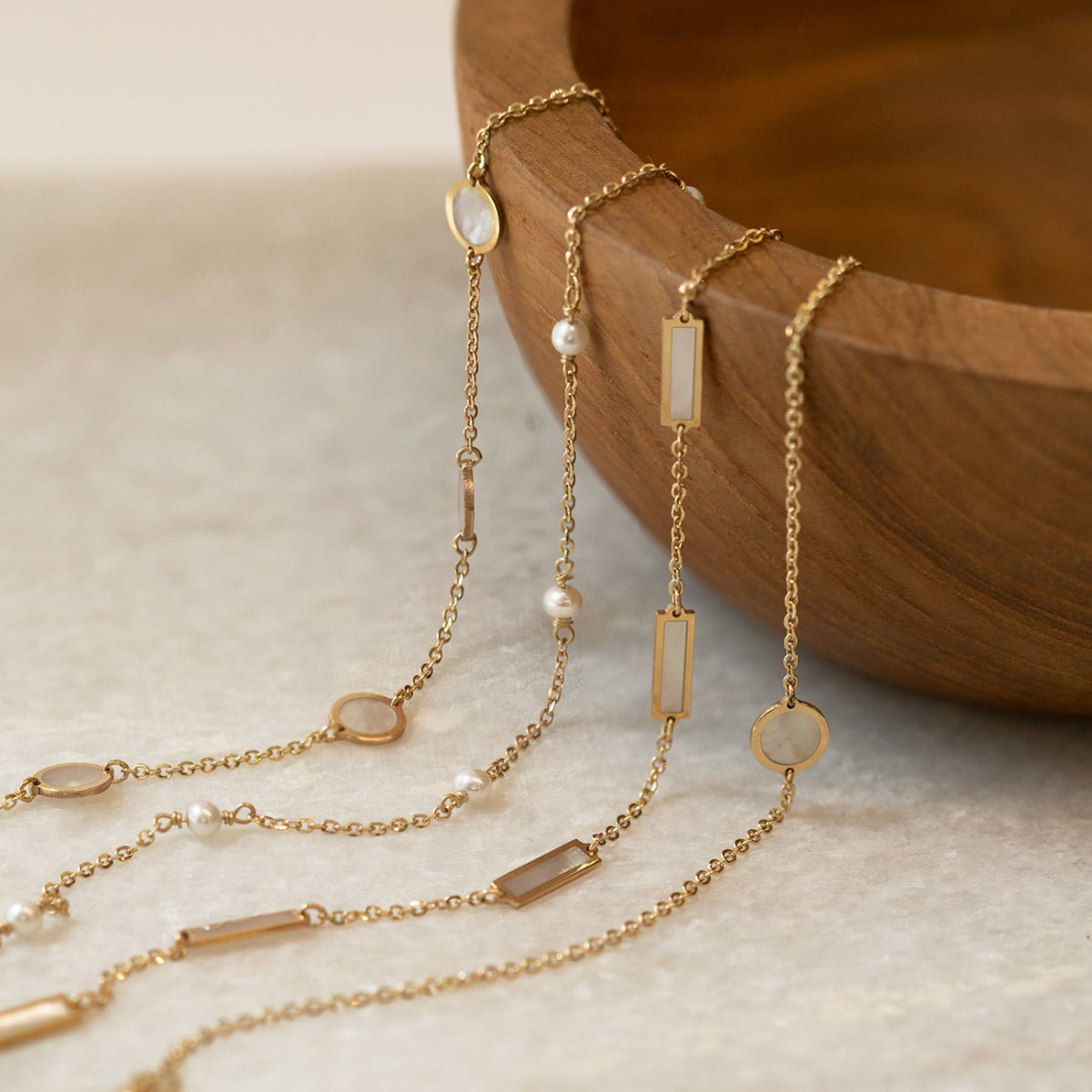 14K gold chain bracelets and necklaces with white mother of pearl discs and bars by a wooden bowl